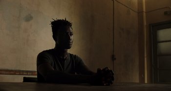 Movie still from “Crimes of the Future” (2022), directed by David Cronenberg – A man sitting at a table in the dark; Close Up shot, Low angle