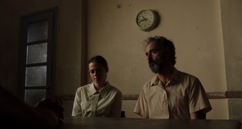 Movie still from “Crimes of the Future” (2022), directed by David Cronenberg – A man and a woman sitting in front of a wall clock; Medium shot, Low angle