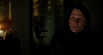 Movie still from “Crimes of the Future” (2022), directed by David Cronenberg – An old man wearing a black robe and a black hood; Close Up shot, Over the shoulder angle
