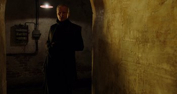 Movie still from “Crimes of the Future” (2022), directed by David Cronenberg – A man in a black coat standing in a dark room; Medium shot, Low angle