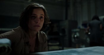 Movie still from “Crimes of the Future” (2022), directed by David Cronenberg – A woman sitting at a table in a dark room; Close Up shot, Low angle