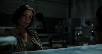 Movie still from “Crimes of the Future” (2022), directed by David Cronenberg – A young woman is standing at a counter; Close Up shot, Over the shoulder angle