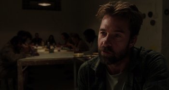 Movie still from “Crimes of the Future” (2022), directed by David Cronenberg – A man with a beard sitting in front of a group of diners; Close Up shot, Over the shoulder angle