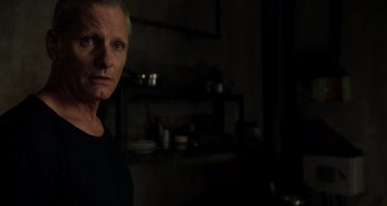 Movie still from “Crimes of the Future” (2022), directed by David Cronenberg – A man standing in a dark room looking at the camera; Close Up shot, Over the shoulder angle