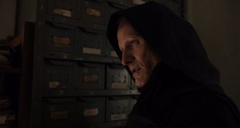 Movie still from “Crimes of the Future” (2022), directed by David Cronenberg – A man in a black robe and a hood is in front of a bunch of drawers; Close Up shot, Low angle