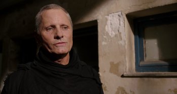 Movie still from “Crimes of the Future” (2022), directed by David Cronenberg – An older man wearing a black shirt in a room with peeling paint; Close Up shot, Low angle