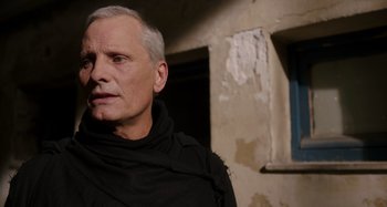 Movie still from “Crimes of the Future” (2022), directed by David Cronenberg – An older man wearing a black shirt and a black scarf; Close Up shot, Over the shoulder angle