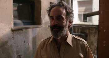 Movie still from “Crimes of the Future” (2022), directed by David Cronenberg – An older man with a beard and grey hair is smiling; Close Up shot, Over the shoulder angle