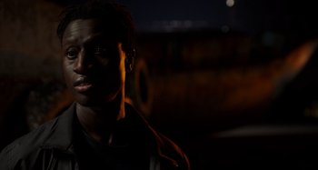 Movie still from “Crimes of the Future” (2022), directed by David Cronenberg – A young man is standing in the dark; Close Up shot, Over the shoulder angle