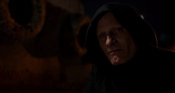 Movie still from “Crimes of the Future” (2022), directed by David Cronenberg – A man in a black hooded jacket looking at the camera; Close Up shot, Low angle