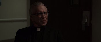 Movie still from “The Conjuring: The Devil Made Me Do It” (2021), directed by Michael Chaves – A man wearing glasses and a priest's outfit; Close Up shot, Over the shoulder angle