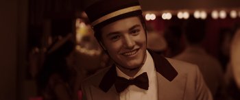 Movie still from “The Conjuring: The Devil Made Me Do It” (2021), directed by Michael Chaves – A man wearing a hat and a bow tie smiling; Close Up shot, Low angle