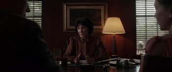 Movie still from “The Conjuring: The Devil Made Me Do It” (2021), directed by Michael Chaves – An older woman sitting at a table in front of a lamp; Medium shot, Over the shoulder angle