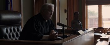 Movie still from “The Conjuring: The Devil Made Me Do It” (2021), directed by Michael Chaves – An older man sitting in front of a microphone in a courtroom; Medium shot, Over the shoulder angle