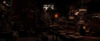 Movie still from “The Conjuring: The Devil Made Me Do It” (2021), directed by Michael Chaves – A man standing next to a stack of books in a room; Wide shot, High angle