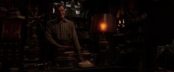 Movie still from “The Conjuring: The Devil Made Me Do It” (2021), directed by Michael Chaves – A man standing in front of a table with books and a tea pot; Medium shot, Low angle