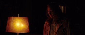 Movie still from “The Conjuring: The Devil Made Me Do It” (2021), directed by Michael Chaves – A woman standing in front of a lamp in a dimly - lit room; Medium shot, Over the shoulder angle
