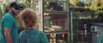 Movie still from “The Conservation Game” (2021), directed by Michael Webber – A woman standing in front of a cage of animals; Close Up shot, Over the shoulder angle