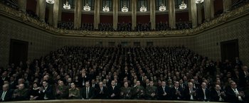 Movie still from “The Courier” (2020), directed by Dominic Cooke – A large group of men in suits sitting in front of an audience; Extreme Wide shot, High angle