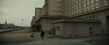 Movie still from “The Courier” (2020), directed by Dominic Cooke – A person walking down a street near a building; Extreme Wide shot, Low angle