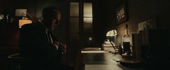 Movie still from “The Courier” (2020), directed by Dominic Cooke – A man sitting at a desk in a dark room; Medium shot, Over the shoulder angle