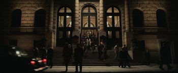 Movie still from “The Courier” (2020), directed by Dominic Cooke – A group of people standing on the steps of a building at night; Extreme Wide shot, High angle