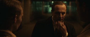Movie still from “The Courier” (2020), directed by Dominic Cooke – A man in a black suit is standing in a dark room; Close Up shot, Low angle