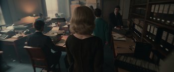 Movie still from “The Courier” (2020), directed by Dominic Cooke – A group of people standing around a room; Medium shot, Over the shoulder angle