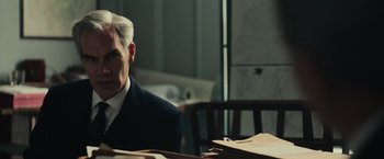 Movie still from “The Courier” (2020), directed by Dominic Cooke – A man sitting at a table in a room; Medium shot, Over the shoulder angle