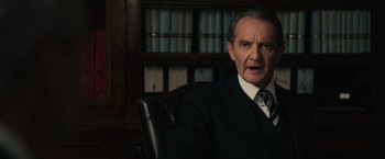 Movie still from “The Courier” (2020), directed by Dominic Cooke – An older man in a suit sitting in an office chair; Close Up shot, Over the shoulder angle