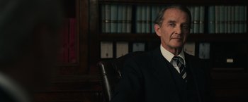 Movie still from “The Courier” (2020), directed by Dominic Cooke – An older man sitting in a chair in front of a book case; Close Up shot, Low angle
