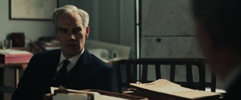 Movie still from “The Courier” (2020), directed by Dominic Cooke – A man sitting at a table in a room; Medium shot, Over the shoulder angle