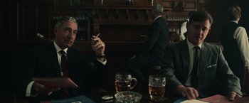 Movie still from “The Courier” (2020), directed by Dominic Cooke – A man sitting at a table smoking a cigarette; Medium shot, Low angle