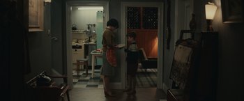 Movie still from “The Courier” (2020), directed by Dominic Cooke – A woman standing next to a young boy in a kitchen; Wide shot, High angle