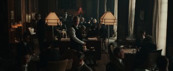 Movie still from “The Courier” (2020), directed by Dominic Cooke – A group of people sitting at tables in a room; Wide shot, High angle