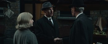 Movie still from “The Courier” (2020), directed by Dominic Cooke – A man wearing a hat and a suit shaking hands with two other men; Medium shot, Over the shoulder angle