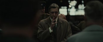 Movie still from “The Courier” (2020), directed by Dominic Cooke – A man smoking a cigarette in front of other men; Close Up shot, Over the shoulder angle