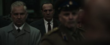 Movie still from “The Courier” (2020), directed by Dominic Cooke – A man in a suit and tie standing next to a man in a uniform; Close Up shot, Over the shoulder angle