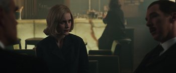 Movie still from “The Courier” (2020), directed by Dominic Cooke – A woman in a black suit sitting in front of a window; Medium shot, Over the shoulder angle