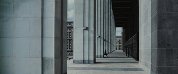 Movie still from “The Courier” (2020), directed by Dominic Cooke – A person walking down a sidewalk near a tall building; Extreme Wide shot, Low angle