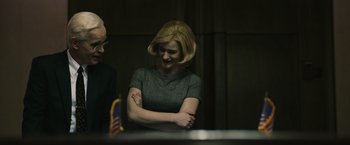 Movie still from “The Courier” (2020), directed by Dominic Cooke – A woman standing in front of a table with an american flag on top of it; Medium shot, Over the shoulder angle