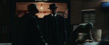 Movie still from “The Courier” (2020), directed by Dominic Cooke – A man wearing a hat and a suit and tie; Medium shot, Over the shoulder angle