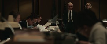 Movie still from “The Courier” (2020), directed by Dominic Cooke – A man standing in front of a table with papers; Medium shot, Over the shoulder angle