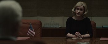 Movie still from “The Courier” (2020), directed by Dominic Cooke – A woman sitting at a table in front of an american flag; Medium shot, Over the shoulder angle