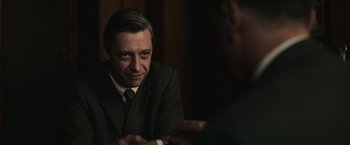 Movie still from “The Courier” (2020), directed by Dominic Cooke – A man wearing a suit and tie sitting in front of another man; Close Up shot, Over the shoulder angle