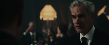 Movie still from “The Courier” (2020), directed by Dominic Cooke – A man in a black suit looking at the camera; Close Up shot, Over the shoulder angle