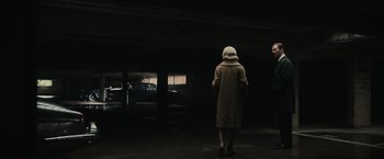 Movie still from “The Courier” (2020), directed by Dominic Cooke – A person in a parking lot wearing a coat and a hood; Wide shot, Low angle