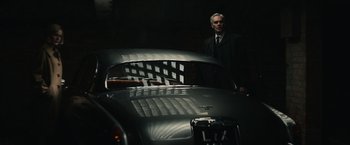 Movie still from “The Courier” (2020), directed by Dominic Cooke – A man standing next to an antique car; Wide shot, Low angle