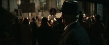 Movie still from “The Courier” (2020), directed by Dominic Cooke – An older man wearing a hat in a crowd of people; Close Up shot, Over the shoulder angle