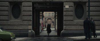 Movie still from “The Courier” (2020), directed by Dominic Cooke – A person walking through an archway in a building; Extreme Wide shot, Over the shoulder angle